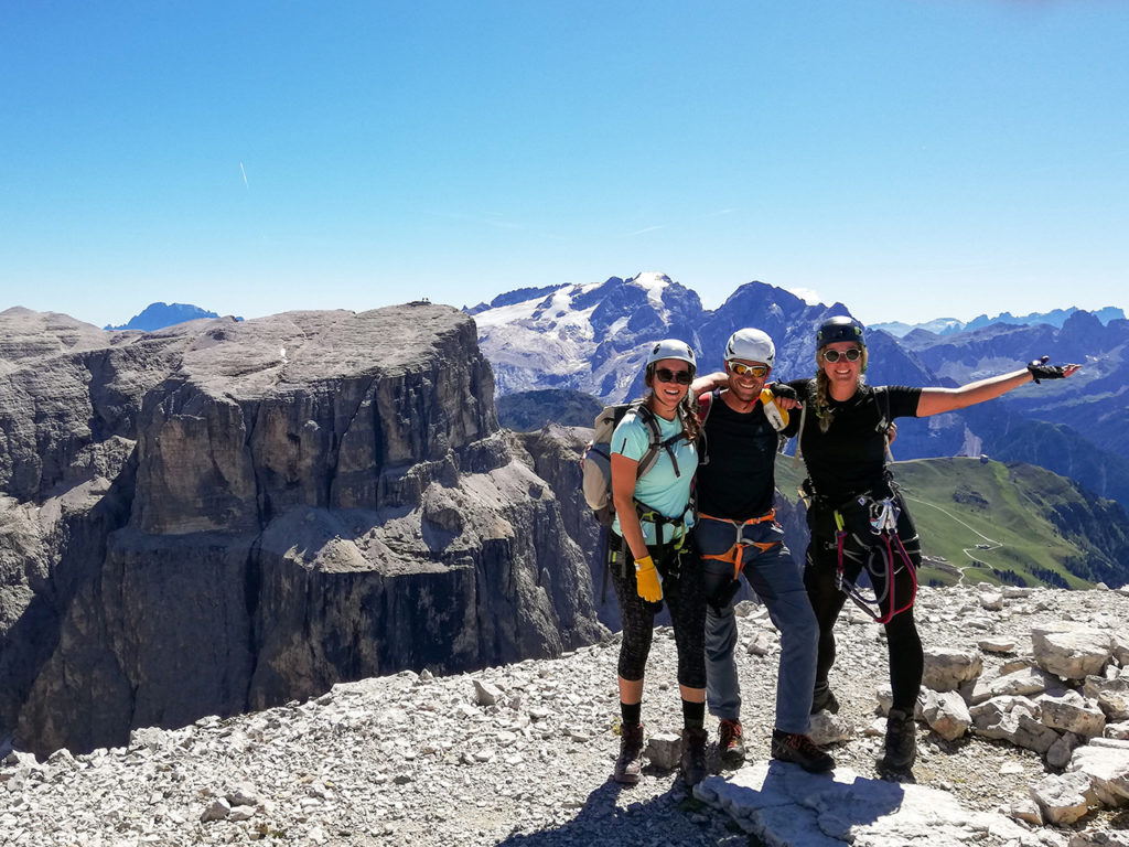 A mountain guide and two female climbers celebrate standing on the summit after a climb